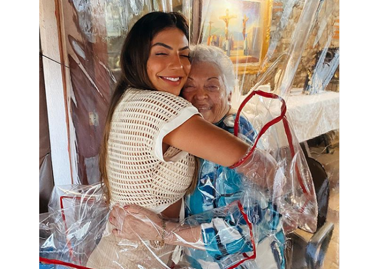 Foto: A blogueira Rachel Apollonio abraçando a avó com um aparato que possibilita abraço sem contato (Reprodução/Instagram)